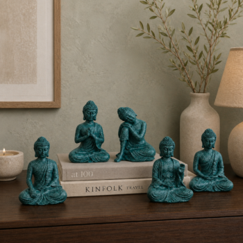 Set of 5 teal Buddha figurines arranged on coffee-table books beside a candle
